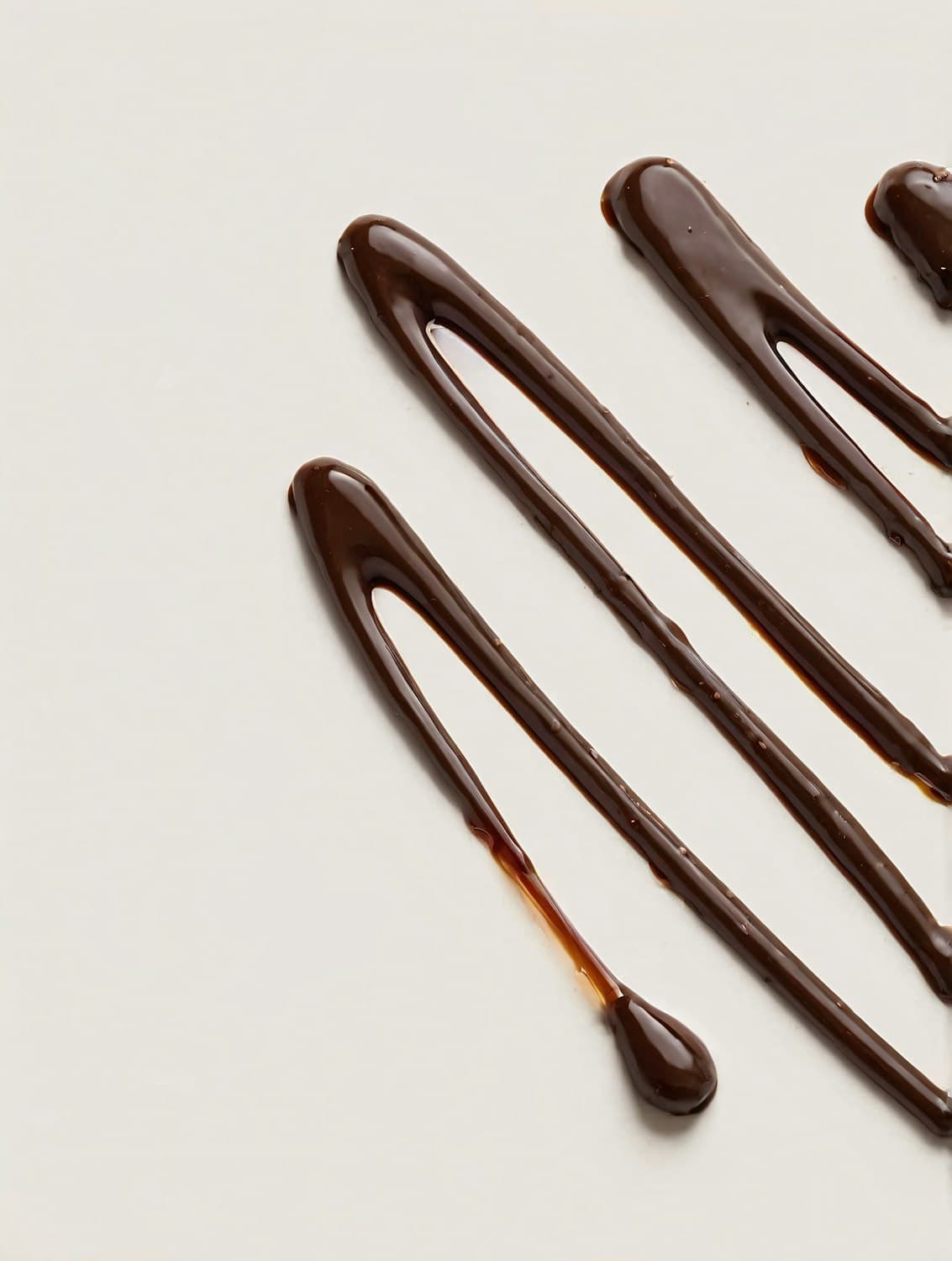 Thick ribbons of glossy tempered chocolate drawn across a pale surface.